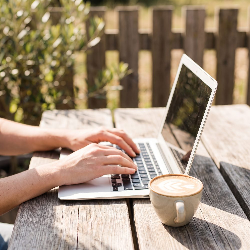 Laptop and coffee on an outdoor table in the sun